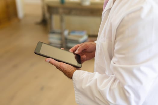 Senior caucasian male doctor using tablet computer in living room. medicine and healthcare services concept.