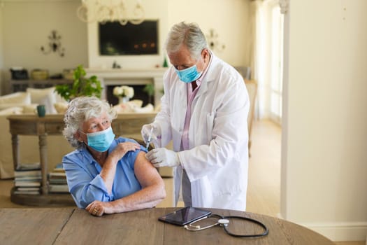 Senior caucasian male doctor vaccinating female patient wearing face masks. medicine and healthcare services during covid 19 pandemic concept.