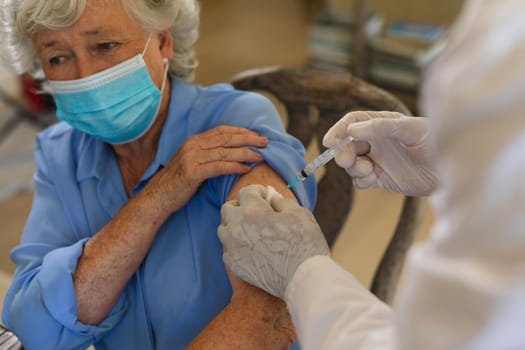 Senior caucasian male doctor vaccinating female patient wearing face mask. medicine and healthcare services during covid 19 pandemic concept.