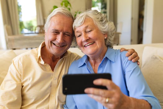 Senior caucasian couple sitting on sofa having video call using smartphone. retreat, retirement and happy senior lifestyle concept.