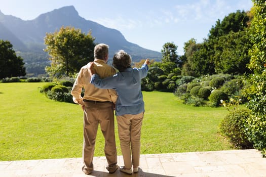 Senior caucasian couple standing and embracing in sunny garden. retreat, retirement and happy senior lifestyle concept.