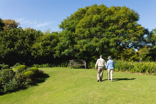 Senior caucasian couple walking together in sunny garden. retreat, retirement and happy senior lifestyle concept.