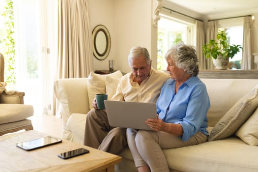 Senior caucasian couple sitting on sofa using laptop. retreat, retirement and happy senior lifestyle concept.