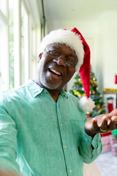 Happy african american senior man wearing santa has having video call at christmas time. christmas, festivity and communication technology.
