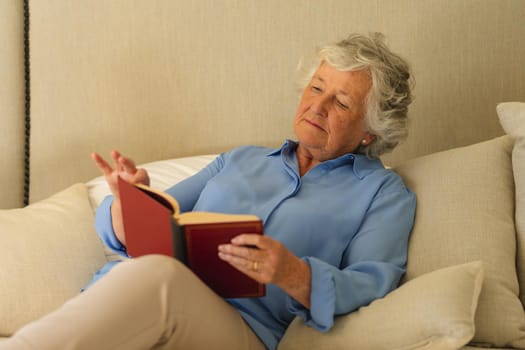 Senior caucasian woman sitting on bed and reading book in bedroom. retreat, retirement and happy senior lifestyle concept.