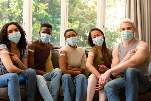 Group of happy diverse female and male friends in face masks showing plasters after vaccination. friendship, health and lifestyle during covid 19 pandemic.