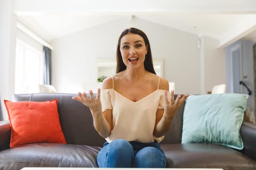 Happy caucasian woman sitting on couch having video call in living room, talking and gesturing. keeping in touch, leisure time at home with communication technology.