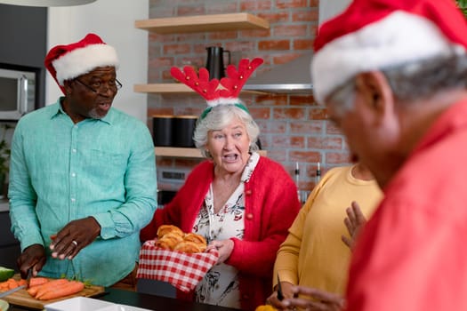 Three diverse senior male and female friends in christmas hats cooking together in kitchen. christmas festivities, celebrating at home with friends.