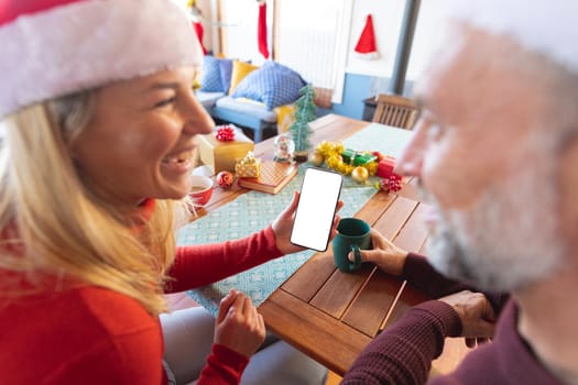 Happy caucasian mature couple making a video call and using smartphone with copy space. christmas, festivity and communication technology.