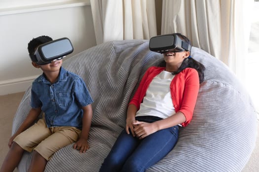 Happy african american boy and girl using vr headsets and smiling at home. childhood with technology, spending free time at home.