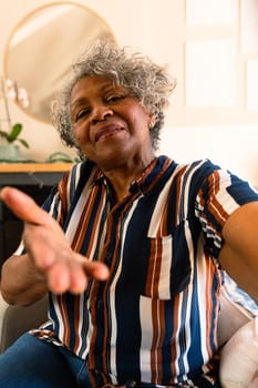 Smiling african american senior woman sitting in armchair and gesturing. healthy retirement lifestyle at home.