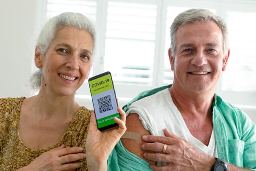 Smiling caucasian senior couple showing smartphone with covid 19 vaccine passport on screen. senior health and lifestyle during covid 19 pandemic.