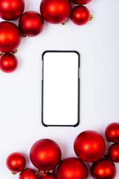 Composition of smartphone with copy space and red baubles on white background. christmas, tradition and celebration concept.