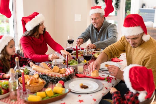 Caucasian multi generation family wearing santa hats having christmas meal. family christmas time and festivity together at home.