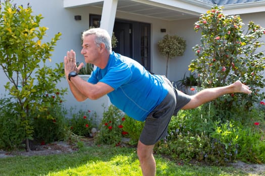 Focused caucasian senior man practicing yoga in garden. active and healthy retirement lifestyle at home and garden.