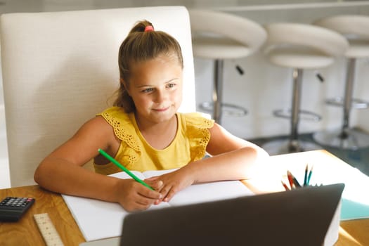 Caucasian girl sitting at table and using laptop during online lessons. childhood education and discovery at at home using technology.