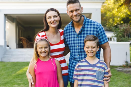 Portrait of smiling caucasian parents with son and daughter outside house embracing in garden. family enjoying leisure time together at home.