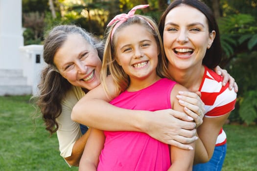 Portrait of smiling caucasian grandmother with adult daughter and granddaughter in garden. multi generation family enjoying leisure time together at home.