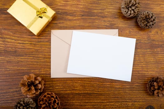 Composition of white card with copy space, envelope and pine cones on wooden background. christmas, communication, tradition and celebration concept.