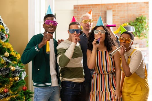 Group of happy diverse female and male friends with whistles and colorful hats celebrating new year. new year, festivities, celebrating at home with friends.