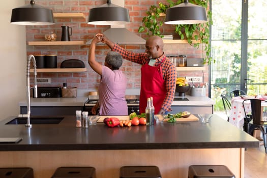 Happy african american senior couple dancing together in kitchen. retirement lifestyle, leisure and spending time at home.