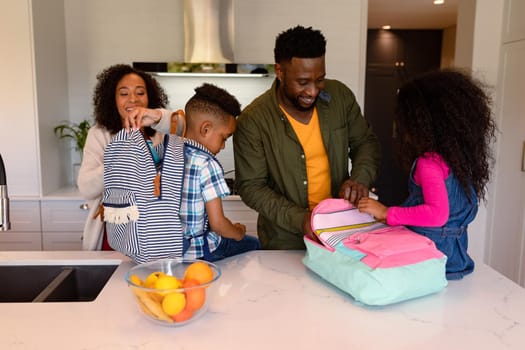 Happy african american parents and children preparing backpacks for school. family time, having fun together at home.