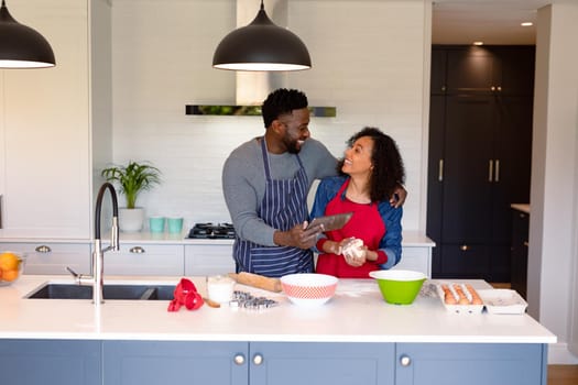 Happy african american couple wearing aprons, baking together and using tablet. family time, having fun together at home.