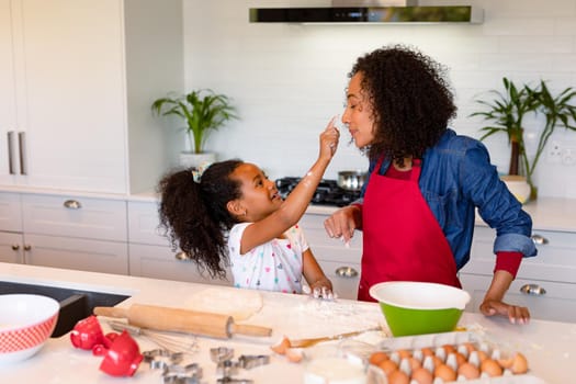 Happy african american mother and daughter baking together in kitchen. family time, having fun together at home.