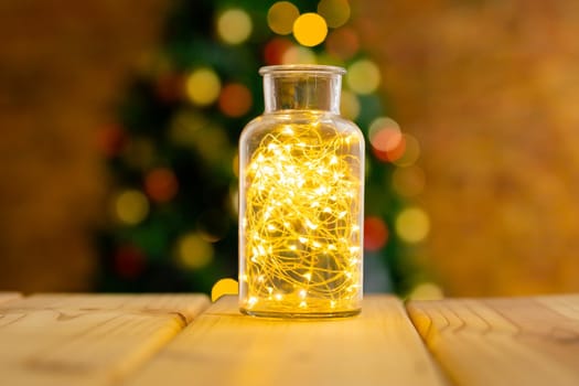 Composition of fairy lights in vase on wooden table with christmas tree and lights in background. christmas, tradition and celebration concept.