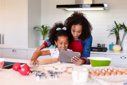 Happy african american mother and daughter baking together in kitchen. family time, having fun together at home.