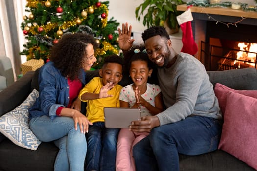 Happy african american family having video call on tablet, christmas decorations in background. christmas, festivity and communication technology.