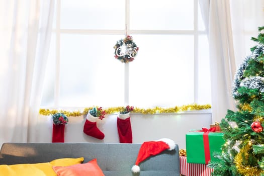 Composition of merry christmas sign in window, with christmas stockings and christmas tree. christmas, tradition and celebration concept.