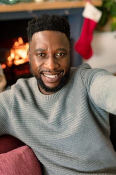 Happy african american man taking selfie, christmas decorations in background. christmas time and festivity at home.