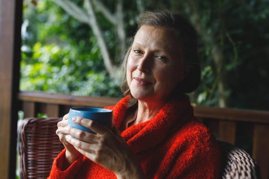 Portrait of happy senior caucasian woman sitting on chair, drinking coffee in garden. retirement lifestyle, spending time alone at home.