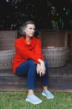 Thoughtful senior caucasian woman sitting and looking away in garden. retirement lifestyle, spending time alone at home.