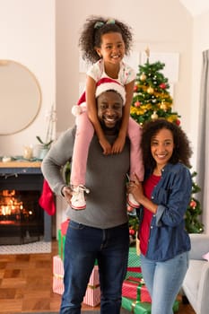 Happy african american parents and daughter looking at camera. family time, christmas, festivity and tradition at home.