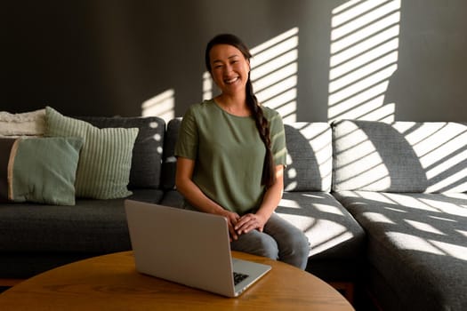 Happy asian woman sitting on sofa at home and using laptop. lifestyle, leisure and spending time at home.