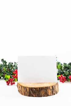 Composition of white card with copy space on log, and branches with berries on white background. christmas, tradition and celebration concept.