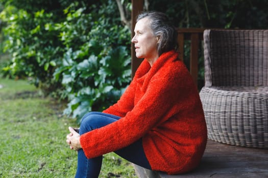 Thoughtful senior caucasian woman sitting and looking away in garden. retirement lifestyle, spending time alone at home.
