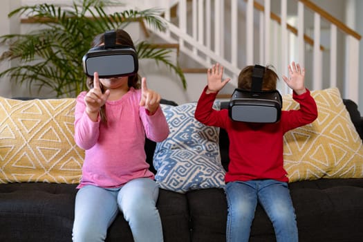 Happy caucasian siblings sitting on sofa, wearing vr headset and having fun. childhood, leisure and discovery using technology at home.