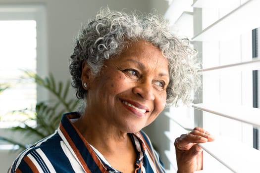 Portrait of smiling african american senior woman looking through window. healthy retirement lifestyle at home.