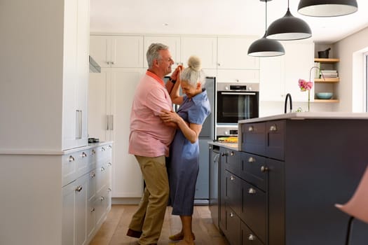 Happy caucasian senior couple dancing together in kitchen and having fun. healthy retirement lifestyle at home.