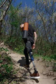a man on a prosthetic leg travels the mountains. Dressed in black jeans and a T-shirt, he carrying mat.