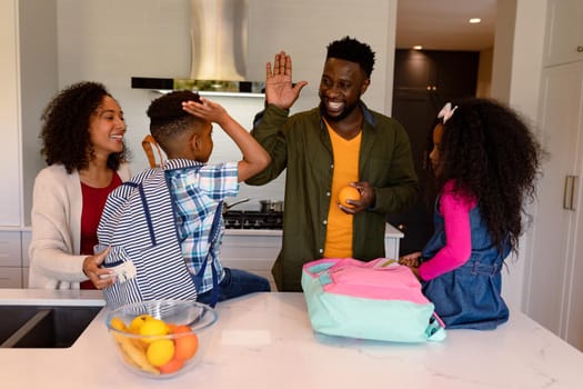 Happy african american parents and children preparing backpacks for school. family time, having fun together at home.