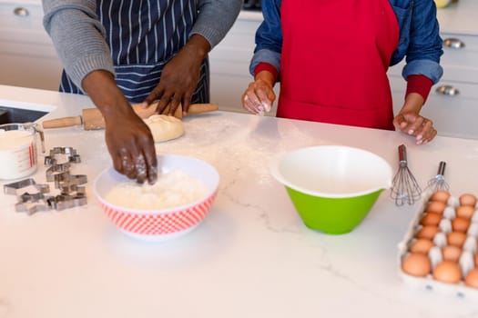 Midsection of african american couple wearing aprons, baking together. family time, having fun together at home.