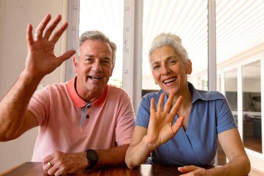 Happy caucasian senior couple having video call, waving to camera. healthy retirement lifestyle at home.