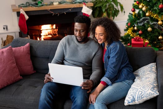Happy african american couple having video call on laptop, christmas decorations in background. christmas, festivity and communication technology.