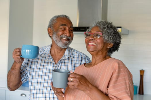 Happy african american senior couple holding mugs with coffee and talking. healthy retirement lifestyle at home.