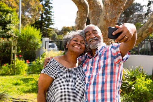 Happy african american senior couple taking selfie in garden. active retirement lifestyle at home and garden.