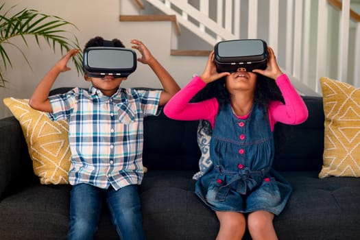 Happy african american siblings sitting on sofa, using vr headset and having fun. childhood, leisure and discovery using technology at home.